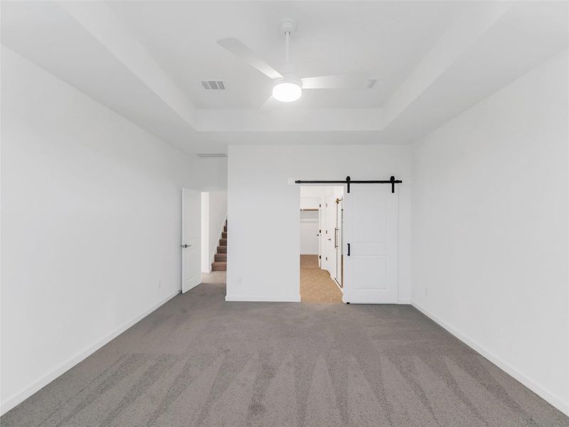 Primary bedroom includes a sliding barn door leading to a closet area, with an adjacent door opening to a stairway. The space is bright and versatile.