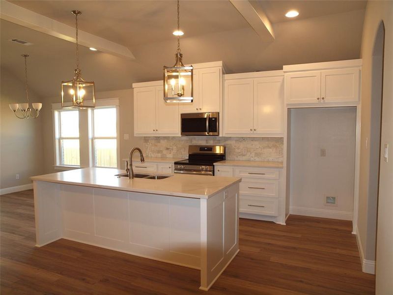 Kitchen with appliances with stainless steel finishes, decorative light fixtures, white cabinetry, sink, and a center island with sink