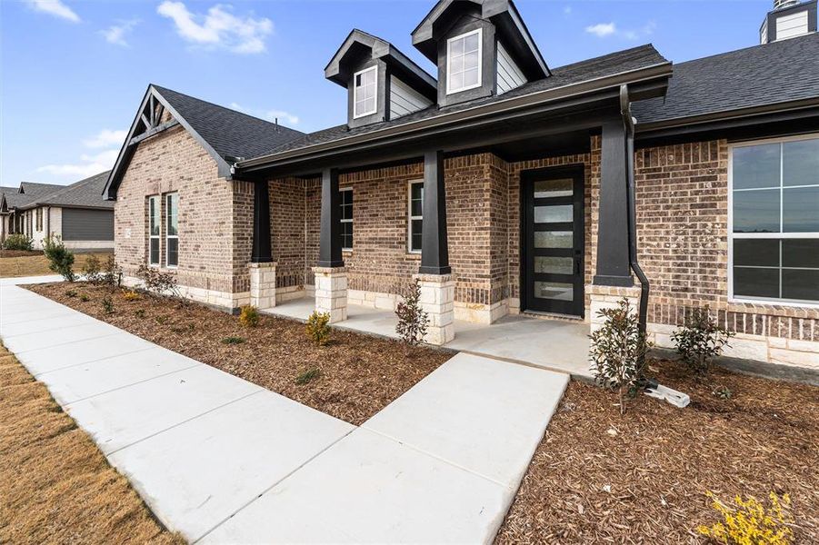 View of front of home featuring covered porch, brick siding, and a shingled roof