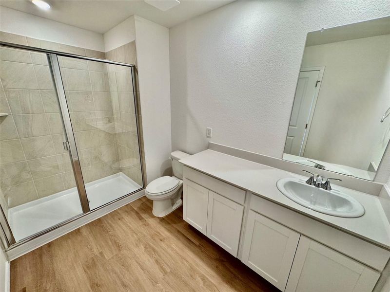 Bathroom featuring a shower stall, vanity, light wood-style flooring, and a textured wall Bathroom featuring a shower stall, vanity, light wood-style flooring, and a textured wall