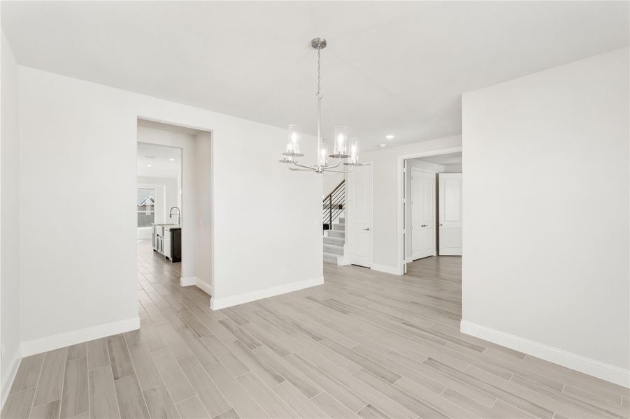 Open dining area with light wood floors, chandelier, and view of staircase and kitchen Open dining area with light wood floors, chandelier, and view of staircase and kitchen