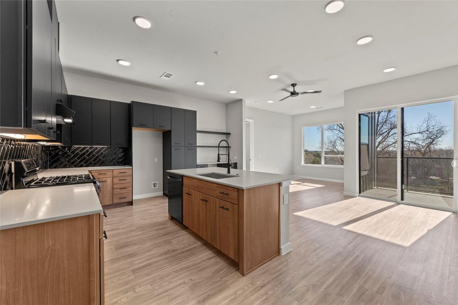 Kitchen with tasteful backsplash, range with gas stovetop, black dishwasher, a kitchen island with sink, and light hardwood / wood-style floors