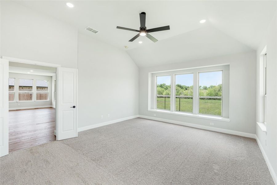 Empty bedroom with vaulted ceiling, ceiling fan, carpet flooring, and large windows overlooking a backyard Empty bedroom with vaulted ceiling, ceiling fan, carpet flooring, and large windows overlooking a backyard