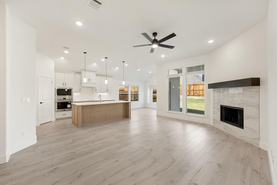 Open-concept living area with hardwood floors, kitchen island, white cabinets, and marble tile fireplace