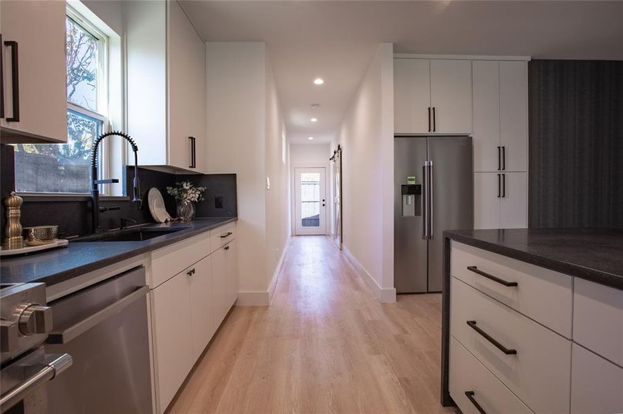 Kitchen with light hardwood / wood-style floors, a barn door, white cabinetry, and appliances with stainless steel finishes