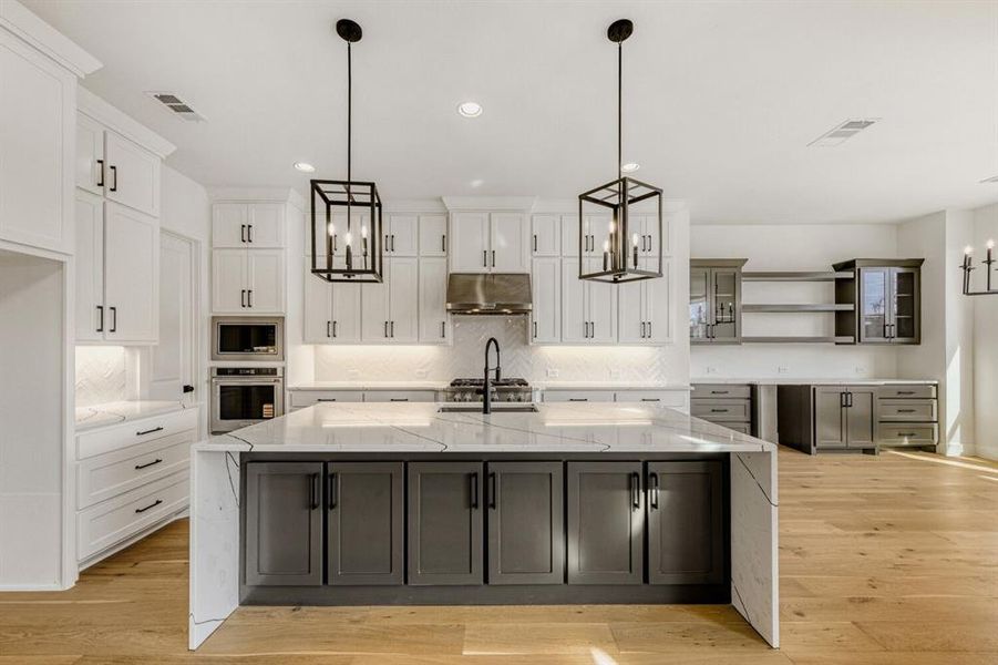 Kitchen featuring open shelves, light stone countertops, hanging lights, and a large island with sink