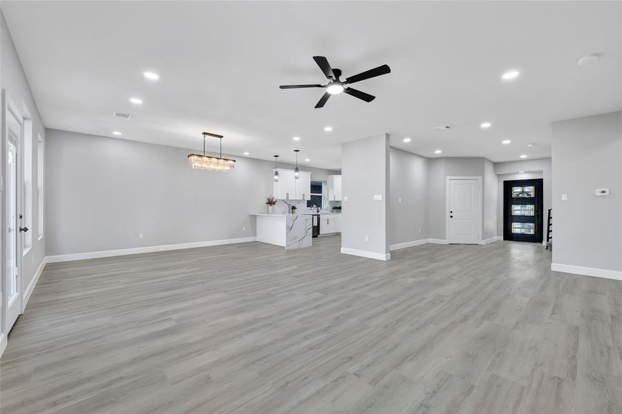 This photo showcases a spacious, open-concept living area with modern gray flooring and neutral walls. It features a sleek kitchen with a large island, contemporary lighting fixtures, and a ceiling fan. Natural light streams in through multiple windows, creating a bright and inviting ambiance.