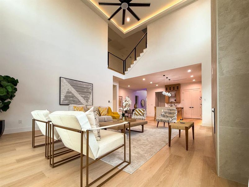 Living room with light wood-style floors, a towering ceiling, recessed lighting, and a ceiling fan