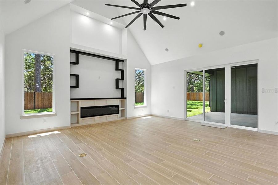 Unfurnished living room with recessed lighting, high vaulted ceiling, light wood-type flooring, a ceiling fan, and a glass covered fireplace Unfurnished living room with recessed lighting, high vaulted ceiling, light wood-type flooring, a ceiling fan, and a glass covered fireplace