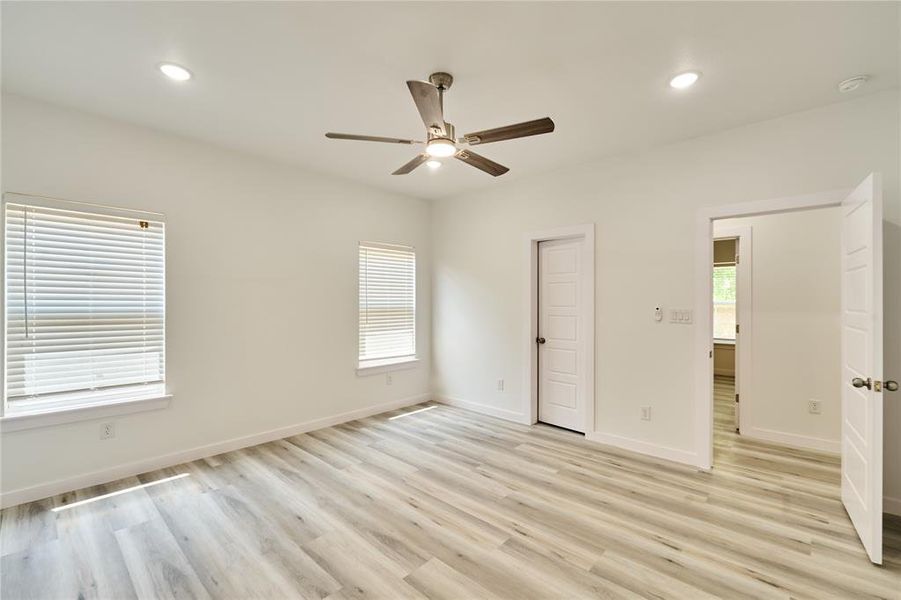 Spacious room featuring wood-finish flooring, two large windows with blinds, and white panel doors