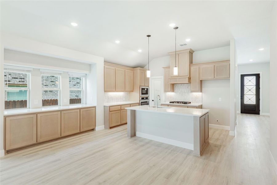 Open kitchen with light wood cabinets, center island, pendant lights, and light hardwood floors