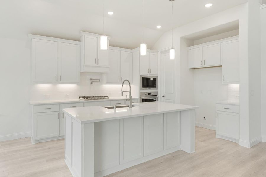 White kitchen with large center island, pendant lights, stainless appliances, and light wood floors