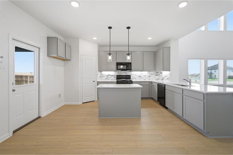 Kitchen with gray cabinetry, a center island, black appliances, and light wood-type flooring