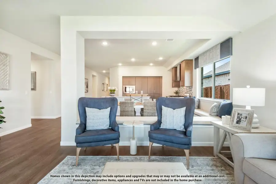 Open-concept living area with two blue accent chairs, hardwood floors, and kitchen visible in background