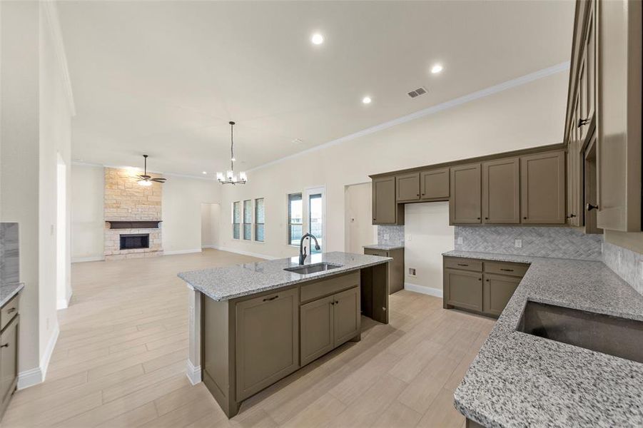 Kitchen with a fireplace, light stone counters, a kitchen island with sink, crown molding, and ceiling fan Kitchen with a fireplace, light stone counters, a kitchen island with sink, crown molding, and ceiling fan