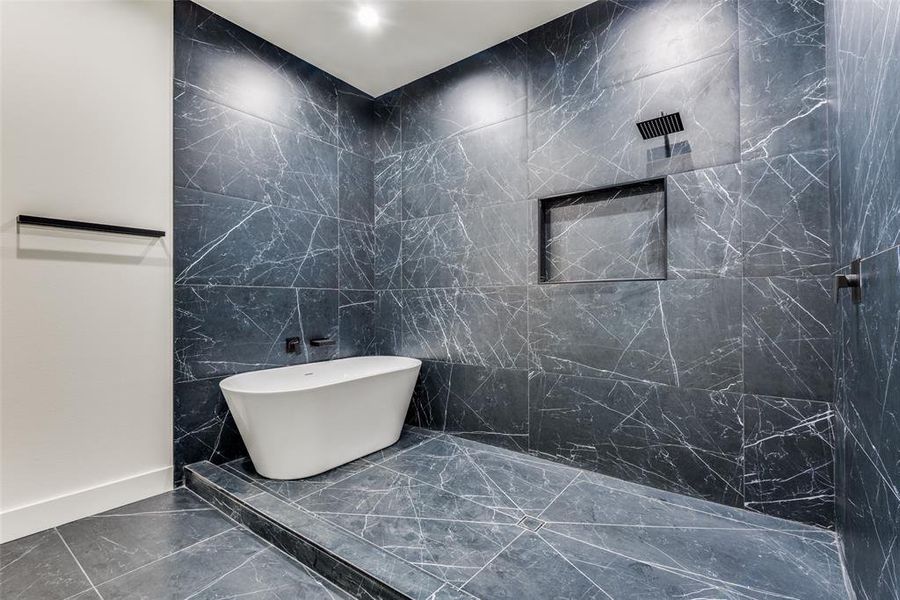 Full bath with tile walls, a freestanding tub, dark marble finish floors, and a marble finish shower