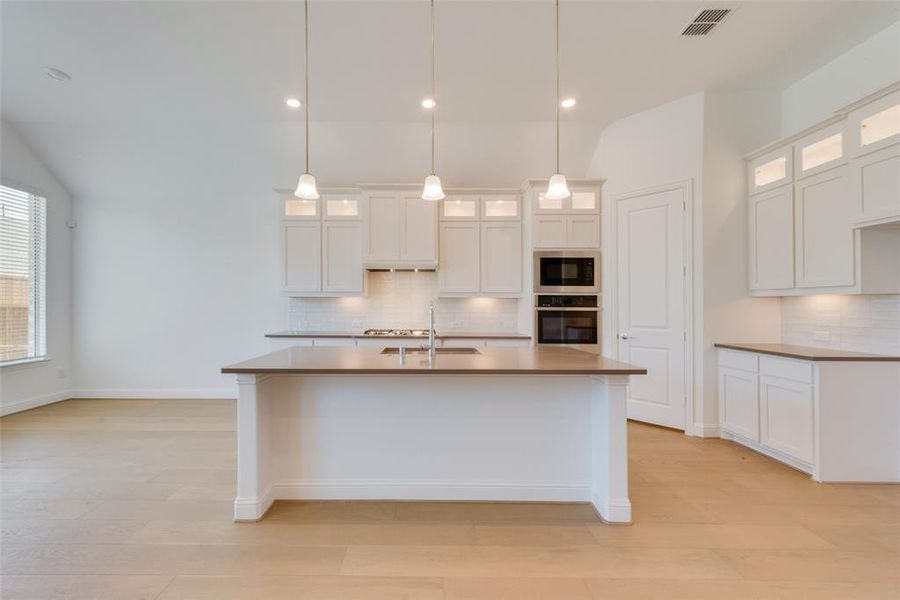 Kitchen featuring white cabinets, decorative backsplash, oven, a center island with sink, and black microwave