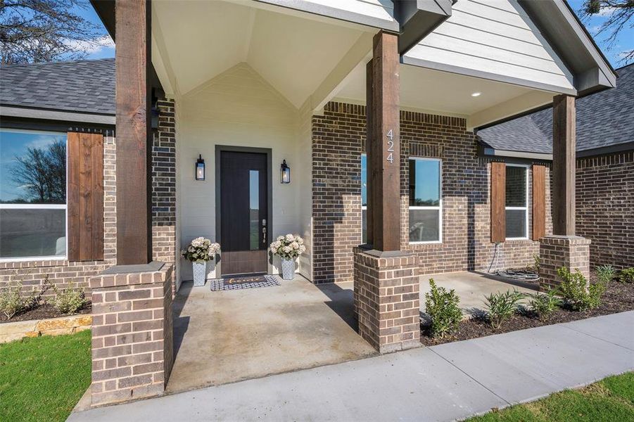 Welcoming covered front porch with impressive architectural details sets the tone for this stunning home. Rich brick facade paired with cedar accents and stained wood columns creates undeniable curb appeal. Vaulted porch ceiling, modern black entry door with glass insert, and coach-style lighting fixtures blend classic craftsmanship with contemporary style.