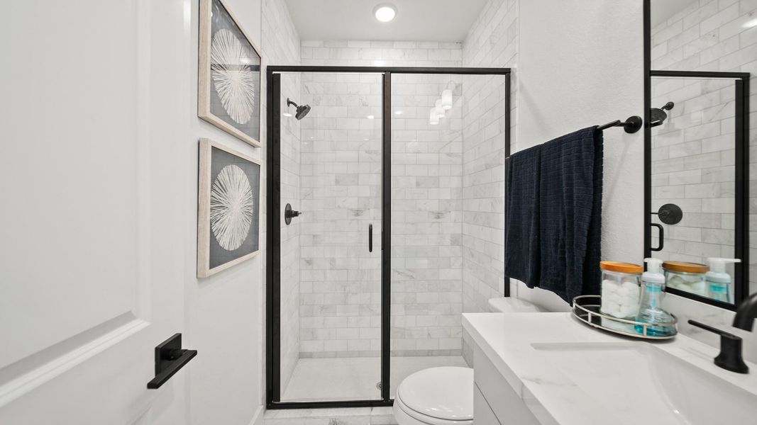 Sophisticatedly refined, this secondary downstairs bathroom boasts a stylish matte black glass-surrounding shower. The marbled-like tile to the ceiling is paired with stately white porcelain countertops and modestly contrasted with grey quality cabinetry. Black hardware gives a notable finish to this bathroom. Sophisticatedly refined, this secondary downstairs bathroom boasts a stylish matte black glass-surrounding shower. The marbled-like tile to the ceiling is paired with stately white porcelain countertops and modestly contrasted with grey quality cabinetry. Black hardware gives a notable finish to this bathroom.
