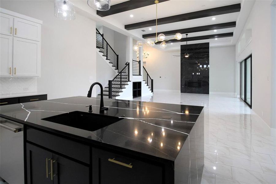 Kitchen featuring white cabinetry, hanging light fixtures, beamed ceiling, dark stone countertops, and a kitchen island with sink