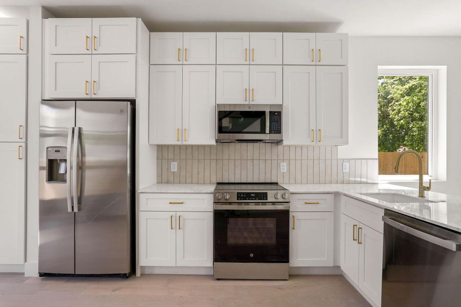 Kitchen featuring white cabinetry, light stone counters, a sink, stainless steel appliances, and backsplash