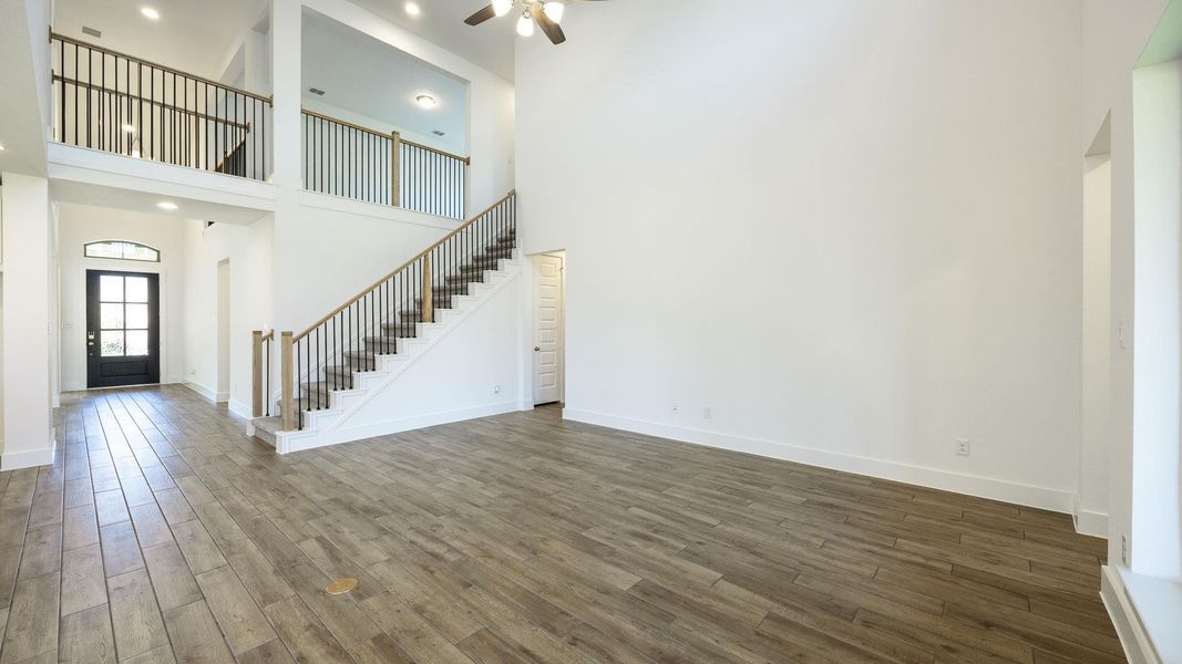 Unfurnished living room featuring ceiling fan, stairs, wood finished floors, and a high ceiling Unfurnished living room featuring ceiling fan, stairs, wood finished floors, and a high ceiling