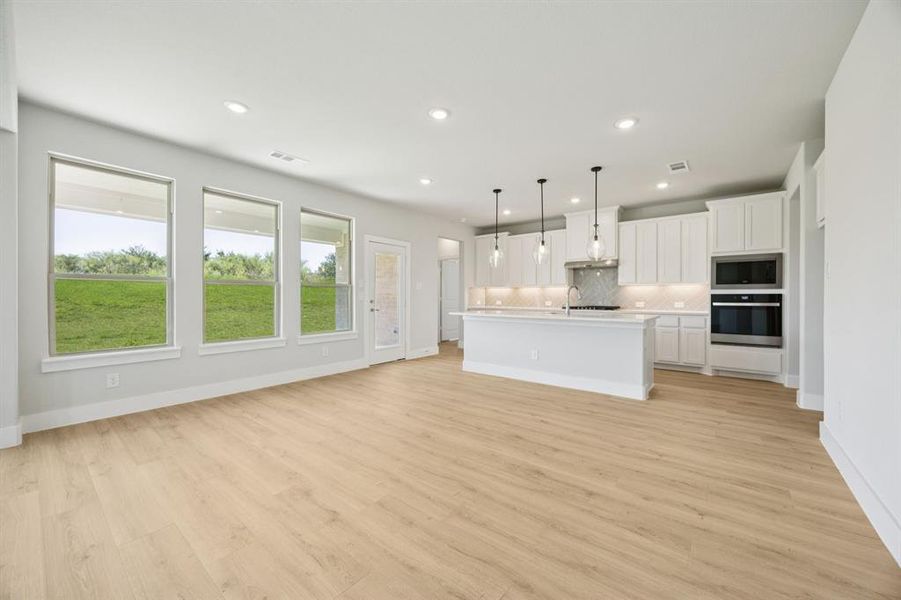 Kitchen featuring white cabinetry, backsplash, decorative light fixtures, appliances with stainless steel finishes, and light countertops
