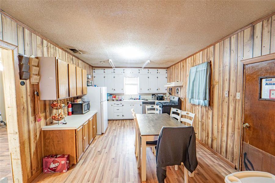 Kitchen featuring light countertops, wooden walls, light wood-type flooring, white cabinetry, and a textured ceiling Kitchen featuring light countertops, wooden walls, light wood-type flooring, white cabinetry, and a textured ceiling