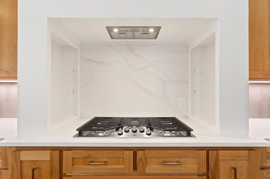 Kitchen featuring brown cabinets, stainless steel gas cooktop, tasteful backsplash, and ventilation hood