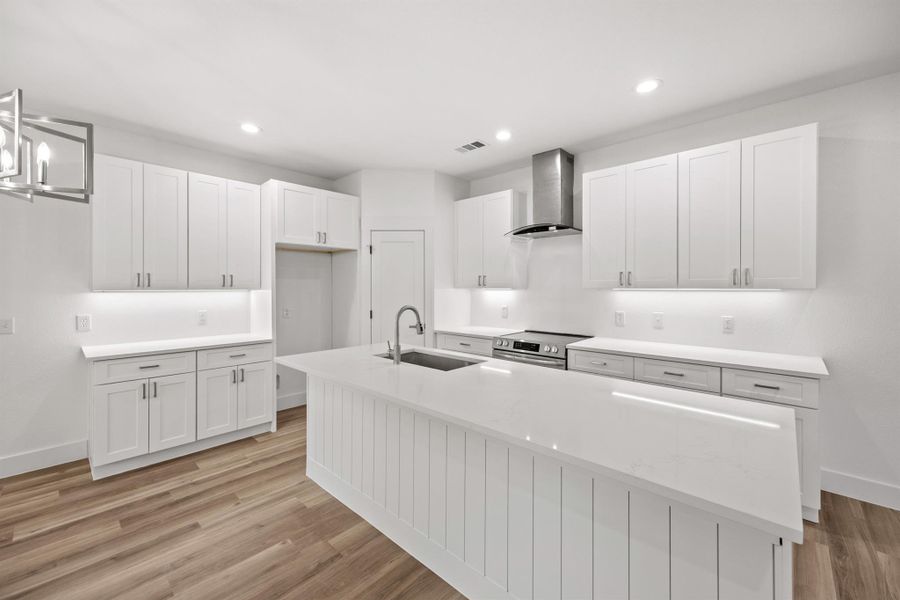 Kitchen featuring white cabinets, an island with sink, light wood finished floors, stainless steel electric range oven, and light stone countertops