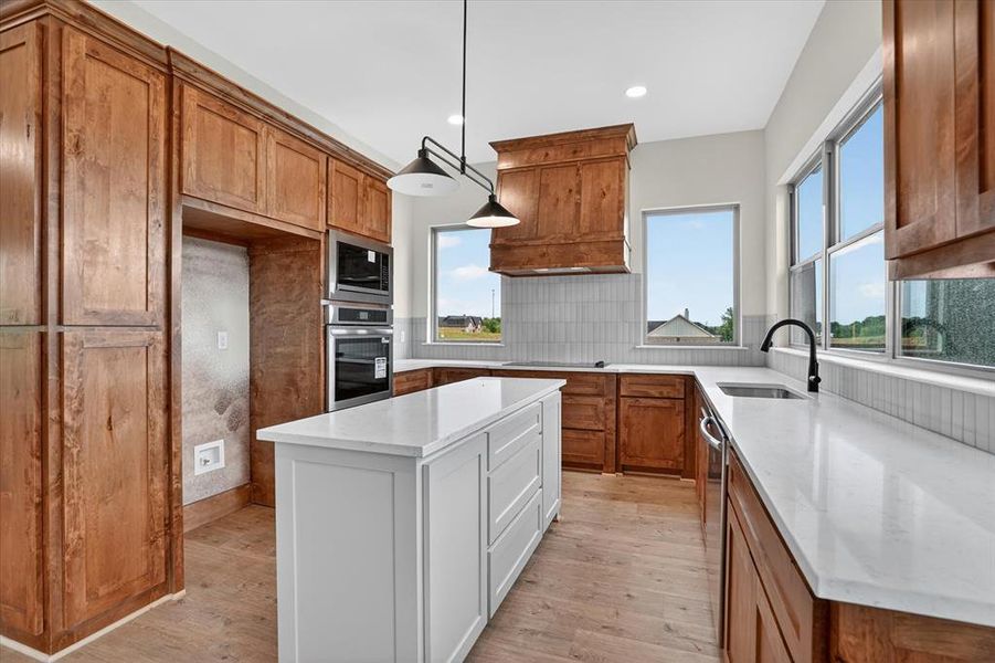 Gourmet kitchen featuring a central island with a white countertop, extensive wood cabinetry, built-in stainless steel appliances, a tile backsplash, and wood-finish flooring