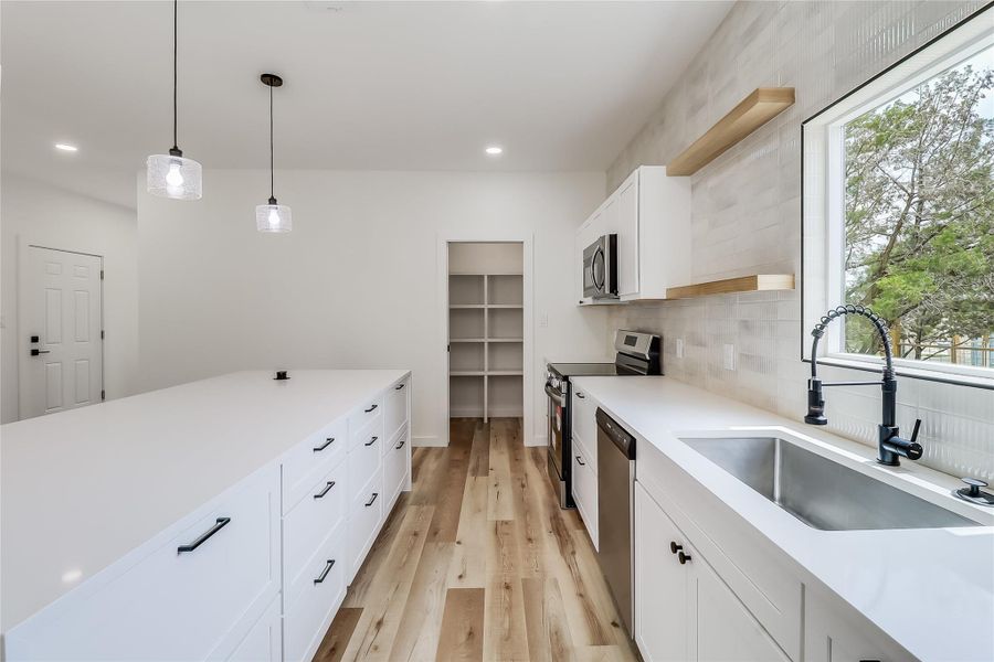 Kitchen featuring light wood finished floors, a sink, decorative backsplash, light countertops, and appliances with stainless steel finishes