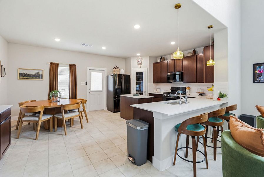 Open-concept kitchen and dining area featuring tile flooring, dark wood cabinetry, a large kitchen island with counter seating, and recessed lighting