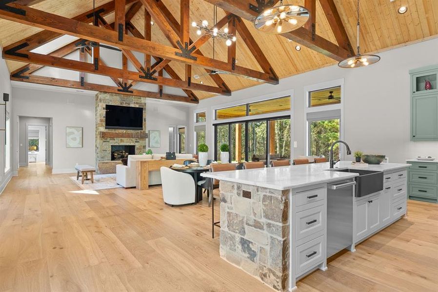 Kitchen featuring a breakfast bar area, a stone fireplace, high vaulted ceiling, light wood finished floors, and a kitchen island with sink