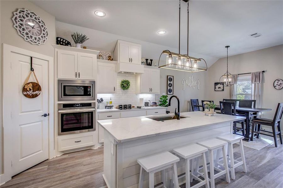 Kitchen with white cabinetry, sink, stainless steel appliances, tasteful backsplash, and an island with sink