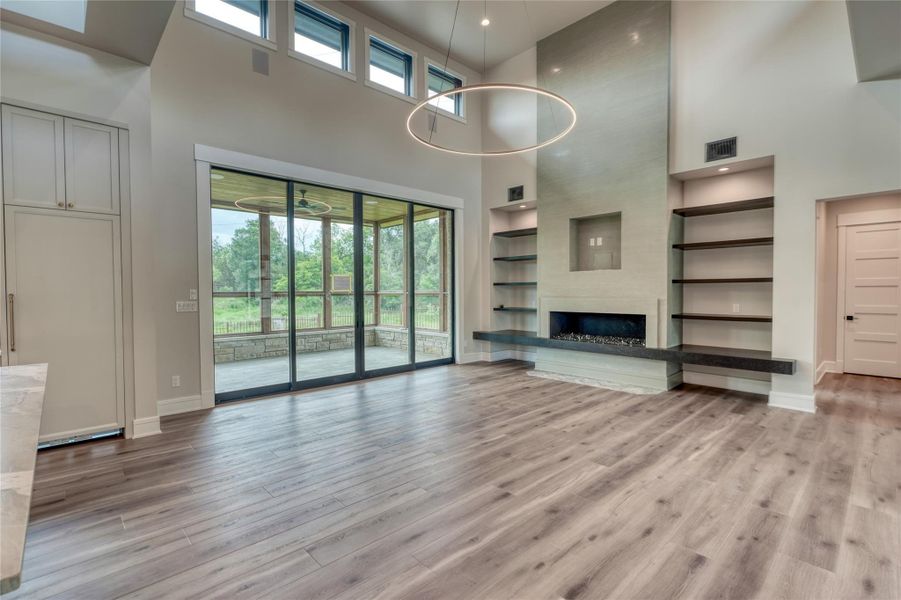Unfurnished living room featuring a high ceiling, built in features, baseboards, light wood-style floors, and a fireplace