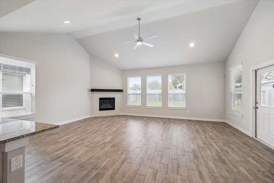 This spacious living room features high ceilings, a modern ceiling fan, and large windows that provide ample natural light. The room has wood-style flooring and a corner fireplace, offering a cozy yet open atmosphere. This spacious living room features high ceilings, a modern ceiling fan, and large windows that provide ample natural light. The room has wood-style flooring and a corner fireplace, offering a cozy yet open atmosphere.