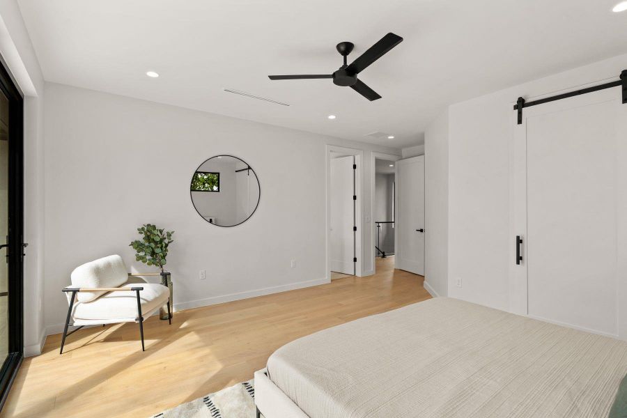 A spacious bedroom features smooth hardwood flooring, sliding barn door, and glass patio doors.