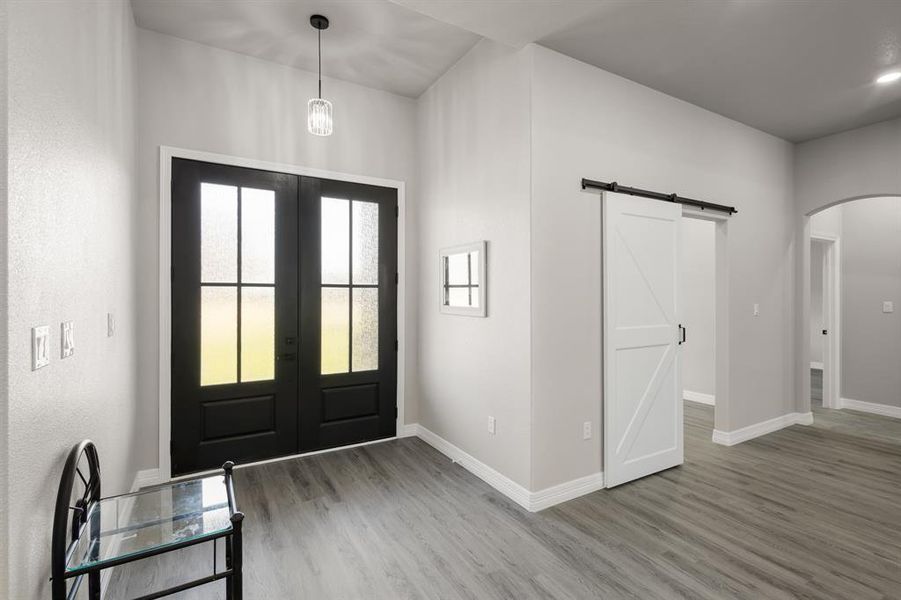 Foyer entrance with arched walkways, a barn door, french doors, and light wood-style flooring