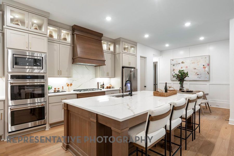 Kitchen with custom range hood, stainless steel appliances, light wood-style flooring, a sink, and an island with sink Kitchen with custom range hood, stainless steel appliances, light wood-style flooring, a sink, and an island with sink