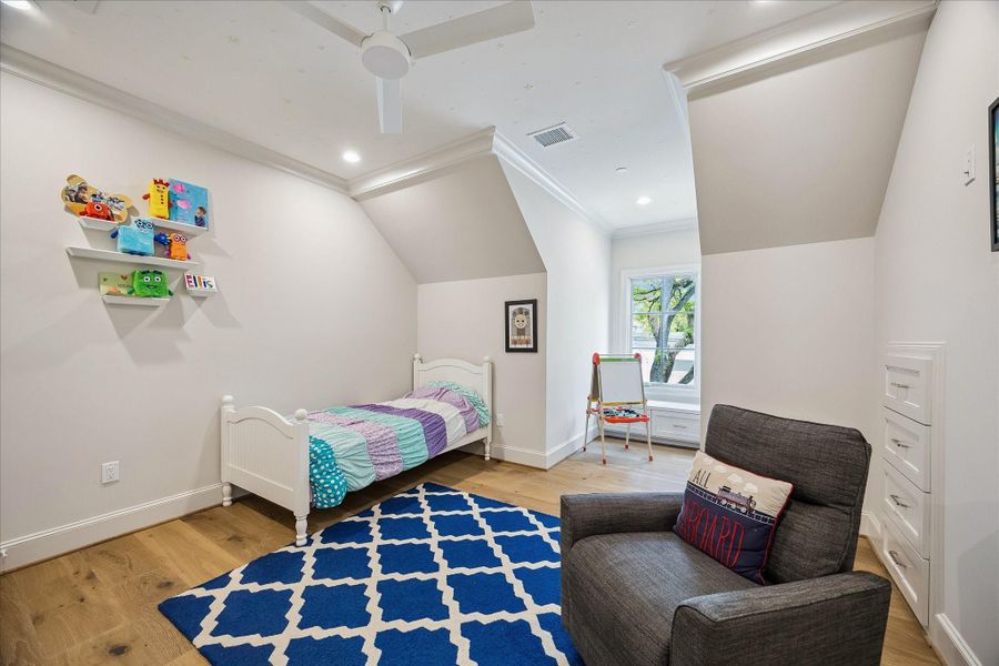 Another charming secondary bedroom featuring crown molding, soft neutral tones, and built-in drawers. Sloped ceiling lines add architectural interest, while natural light through the window fills the space and creates a cozy nook with a built-in window bench.