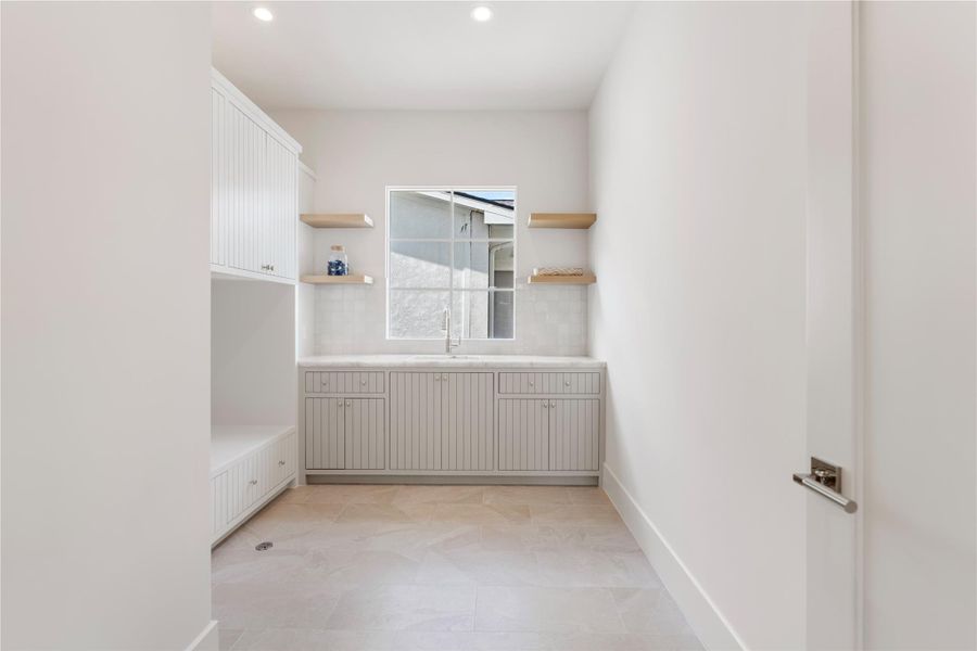 The lavish laundry room, with two white oak shelves and a huge window! The assortment of cabinets, drawers, and shelves will house detergents, dryer balls, and more. Brazilian slate flooring and quartzite countertops continue the fabulous feel. Front loading washer and dryer can be installed at the correct height, with built-in storage beneath.