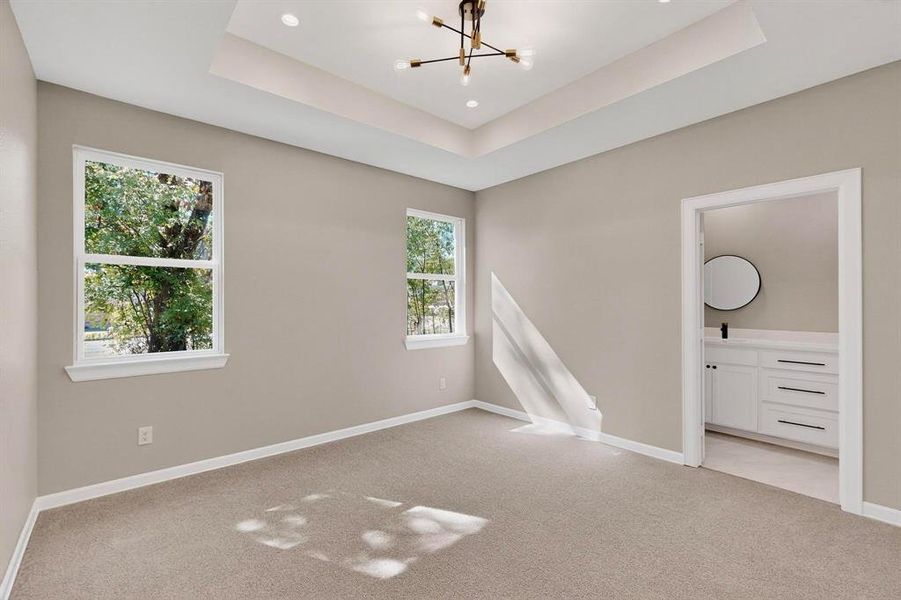 Empty room with a chandelier, light colored carpet, a raised ceiling, and recessed lighting Empty room with a chandelier, light colored carpet, a raised ceiling, and recessed lighting