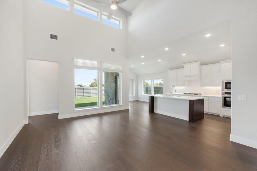 Open-concept living area with high ceilings, dark hardwood floors, and white kitchen with island Open-concept living area with high ceilings, dark hardwood floors, and white kitchen with island