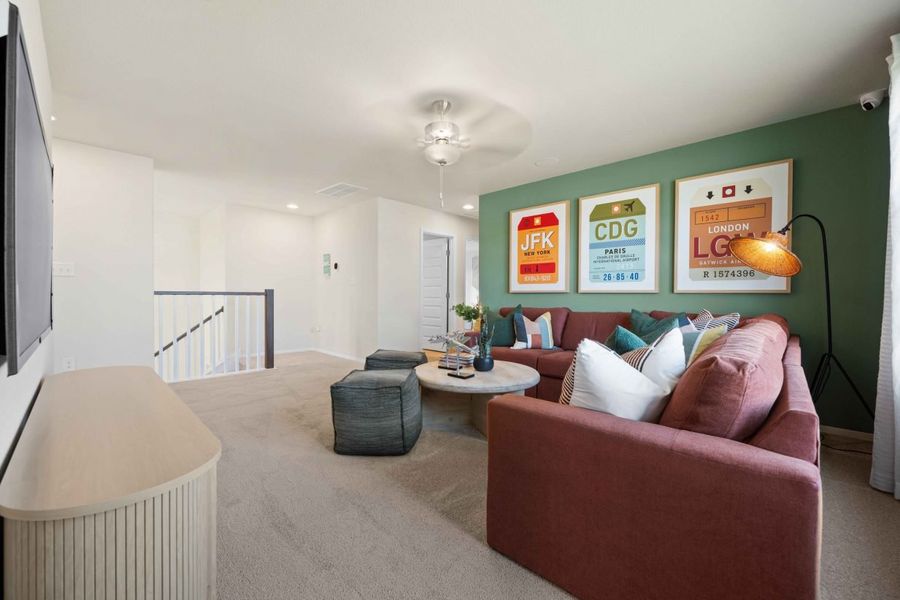 An interior room with windows, brown carpet, green painted walls, a maroon couch, with colorful art and pillows.