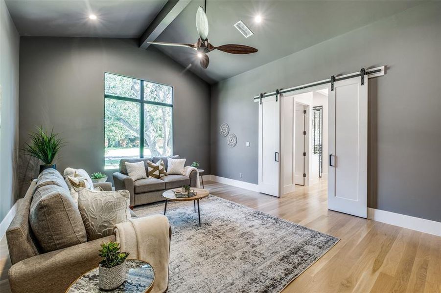 Living room featuring lofted ceiling with beams, ceiling fan, a barn door, and light hardwood / wood-style floors