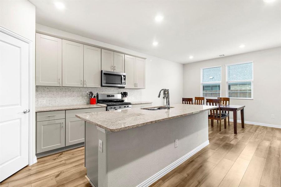 Kitchen featuring appliances with stainless steel finishes, light wood-style floors, an island with sink, tasteful backsplash, and light stone countertops Kitchen featuring appliances with stainless steel finishes, light wood-style floors, an island with sink, tasteful backsplash, and light stone countertops