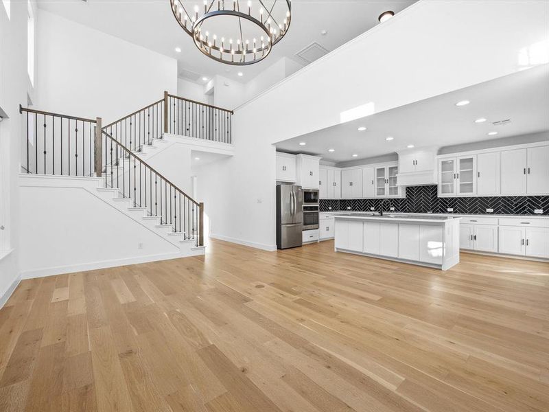 Unfurnished living room with stairs, light wood-style floors, a chandelier, and a towering ceiling Unfurnished living room with stairs, light wood-style floors, a chandelier, and a towering ceiling