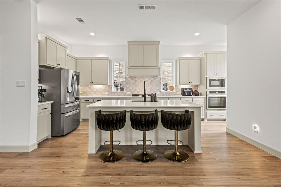 Kitchen with stainless steel appliances, a kitchen island with sink, tasteful backsplash, light countertops, and a kitchen bar