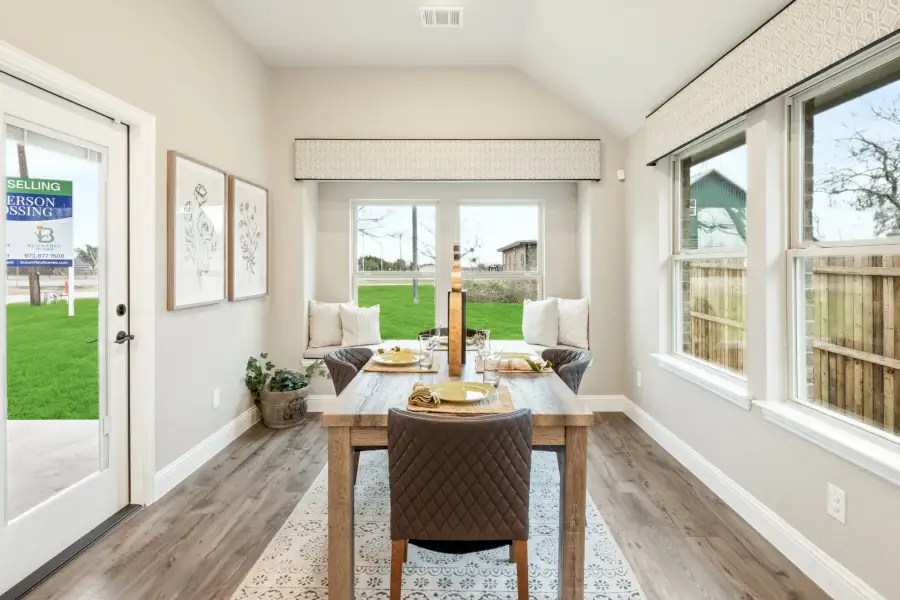 Dining nook with wood table, built-in bench seating, vaulted ceiling, and hardwood floors near large windows
